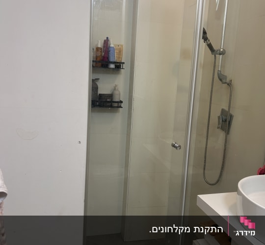 מקלחון זכוכית שקופה מותקן בחדר רחצה עם דלת ציר